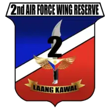 A shield-style crest primarily in red and blue, divided with a diagonal white bar. The centre contains an symbolic military knife with the number '2' covering its blade. The crest is headed by '2nd Air Force Wing Reserve' in all-upper-case letters. Below the knife is a yellow banner for its motto containing the phrase 'Laang Kawal'.