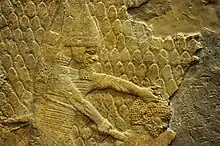 Wall relief from Ninevah featuring an Assyrian soldier, about to behead a prisoner from the city of Lachish. 700-692 BCE. Currently housed in the British Museum