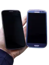 Photo of two phones turned off held next to each other with warm yellow ambience lightning. The phones are rested on a person's hand.
