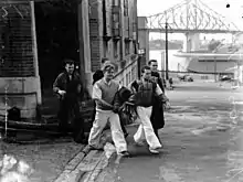 Black and white photograph of five men walking out of a building