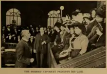 A photograph depicts a jury box full of women in elaborate hats and other early 20th century fashions