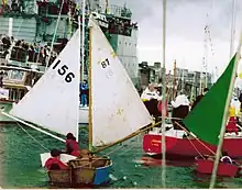 Three small wooden sailing boats behind a yacht sail up a river.