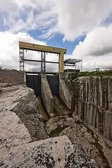 Image d'un ouvrage en béton avec des vannes et dont la partie la plus basse ressemble à un saut à ski qui mène à un corridor en roc.