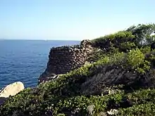 Photographie couleur de vestiges d'une tour ronde vue de profil surplomblant la mer.