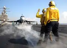 Avion sur le pont d'envol, en train de suivre les indications de deux veilleurs.
