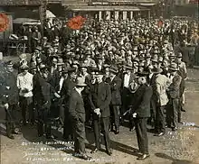Photographie d'un groupe de manifestants en costumes avec des chapeaux entourés par quelques policiers