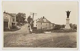 1940, routes de terre battue et trottoirs de bois, rue Principale (route 159) à l'intersection de la rue de l'Église