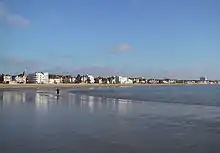 Photographie montrant une grande plage de sable fin de forme courbe à marée basse