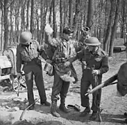 Photo noir et blanc montrant deux hommes en uniforme en train d'en fouiller un troisième, qui garde les mains en l'air.