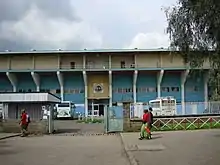 Vue extérieure de l'entrée du stade. Un portail ouvert figure au premier plan.