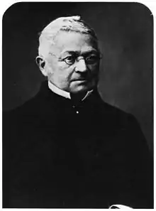 Photographie en noir et blanc d'Adolphe Thiers, haut du corps seulement. Il arbore un habit entièrement noir qui fait ressortir ses cheveux blancs et son visage. Il porte ses petites lunettes ovales.