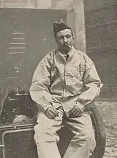 Photographie d'un homme fumant une cigarette assis sur une table.