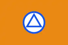 Reproduction en couleurs de l'emblème du VNV. Sur un fond orange, un triangle aux contours bleu est inséré dans un cercle blanc