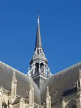 Grande flèche de bois surmontée d'une croix. En arrière-plan, un ciel bleu avec un oiseau.