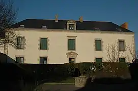 Vue d’un édifice à deux étages de cinq fenêtres, aux volets verts clos .