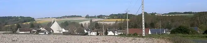 Photographie en couleur d'un alignement de maisons dont émerge le pignon d'une église moderne.