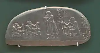 Plaque en pierre aux formes arrondies avec des personnages et des signes gravés.