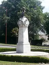 Photographie en couleurs d'un buste en métal sur un piédestal de pierre.