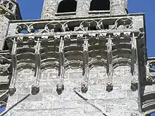 Gros plan en contre-plongée. On voit les arcatures qui soutiennent le rebord de la plate-forme, et la balustrade de celle-ci.