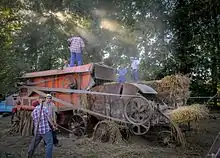 Photographie en couleurs de personnages s'affairant autour de matériels agricoles.