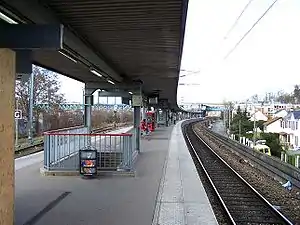 Le quai central de la gare de Conflans-Fin-d'Oise, vu en direction de Cergy. On distingue au fond le viaduc de la ligne de Paris à Mantes par Conflans, qui offre une correspondance.