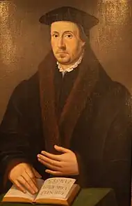 Huile sur toile, couleurs dominantes marron et noir, portrait d’un homme de face, portant une coiffe et revêtu d'un manteau bordé de fourrure ; sa main droite est posée sur un livre ouvert où figure son nom