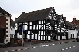Photo d'une maison aux murs blancs avec des poutres en bois apparentes, située à un carrefour