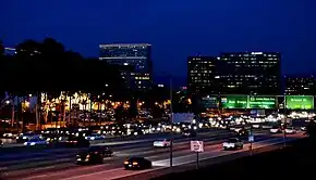 On aperçoit des panneaux en direction de San Diego et d'Anaheim notamment. Immeubles et palmiers à l'arrière-plan.