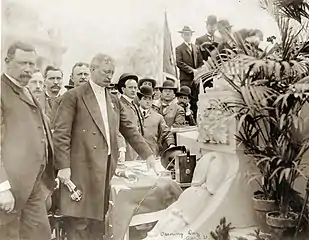 Photographie sépia d'un homme entouré d'une foule appuyant sur un bouton