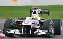 Photographie d'une monoplace blanche, quasiment vue de face, vue dans un virage, tournant à droite.