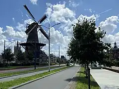 Photographie en couleurs d'une route traversant une ville, un moulin et des bâtiments constrits sur sa gauche.