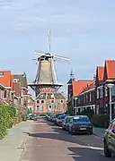 Photographie en couleurs d'une rue entourée de maisons, un moulin apparaissant à son extrémité.