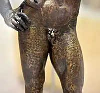 Inscription bilingue. Hercule de Séleucie du Tigre. Statuette, bronze, IIe&nbsp;siècle EC, H. 85,5 cm., d'après un original attribué à Lysippe jeune. Musée national d'Irak. Bagdad