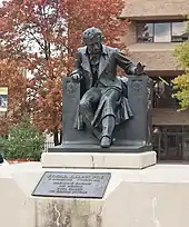 Statue d'un homme assis sur une chaise posée sur un socle de pierre au milieu d'un parc