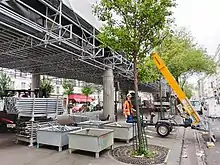 Échafaudage suspendu permettant aux ouvriers de travailler sous le tablier du métro aérien sans que l'installation ne gène les activités citadines comme la tenue du marché de Grenelle.