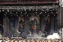 Un groupe de musique joue de jour sur une grande scène devant un public