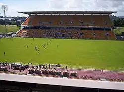 vue d'un stade depuis une tribune avec au premier plan une pelouse et au second-plan une tribune couvertes à deux étages
