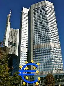 Gratte-ciel de l'Eurotower, 40&nbsp;étages ; d'autres grattes-ciel plus petits sont visibles sur la gauche. En bas de la tour, une sculpture bleue du symbole de l'euro autour et dans lequel se trouvent onze étoiles jaune.