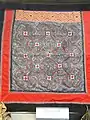 Porte-bébé Miao. Broderie et tissage façonné tujia sur galons encadrant un carré d'impressions à la cire (batik Miao). Yunnan Nationalities Museum (en), Kunming.