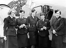 Photo noir et blanc de cinq femmes en uniforme (trois ont un calot, une porte une casquette) posant devant un avion.