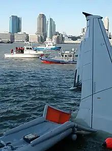 Photo de l'avion amarrée sur la rive. La photo, prise depuis l'intérieur de l'avion, montre l'aile et un toboggan d'évacuation ainsi que la ville de New York à l'arrière-plan.