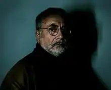 Photographie d'un homme barbu et portant des lunettes, vu de profil, le regard tourné vers l'objectif.