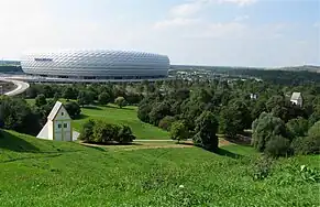 Fröttmaninger Berg, à gauche l'installation artistique « Village englouti », à droite l'église Heilig-Kreuz&nbsp;(de), à l'arrière l'Allianz Arena.