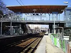 Photographie couleur. Voies et quais enjambés par une passerelle. Sur un quai : barrières de chantier.