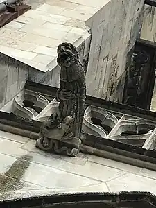 Gargouille représentant un moine barbu semblant terrifié. À ses pieds, un dragon menaçant.