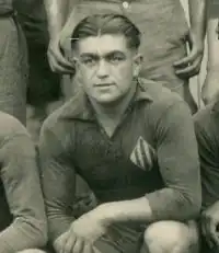 Photographie noir et blanc : c'est un portait d'un homme en maillot de sport qui regarde devant lui.