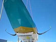 Vue du dessous du bateau, depuis l'avant, en contre-plongée. Les foils se détachent sur le ciel.