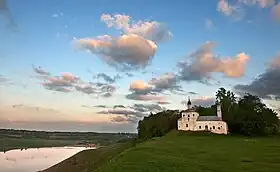 Photographie prise à la tombée de la nuit montrant une église à droite dominant un paysage avec un lac en bas à gauche.