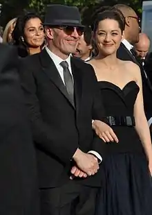  Photographie en couleurs de quatre personnes vêtues élégamment, dont un enfant, sur un grand escalier au tapis rouge.