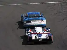 Photographie de deux voitures de grand tourisme et de sport-prototype, l'une derrière l'autre, vue de derrière